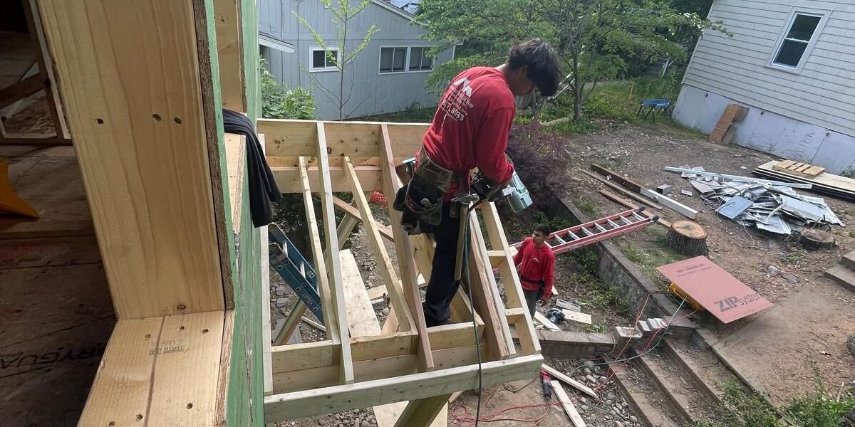 Carpenter framing a custom structural room addition and floor joist system on residential construction site