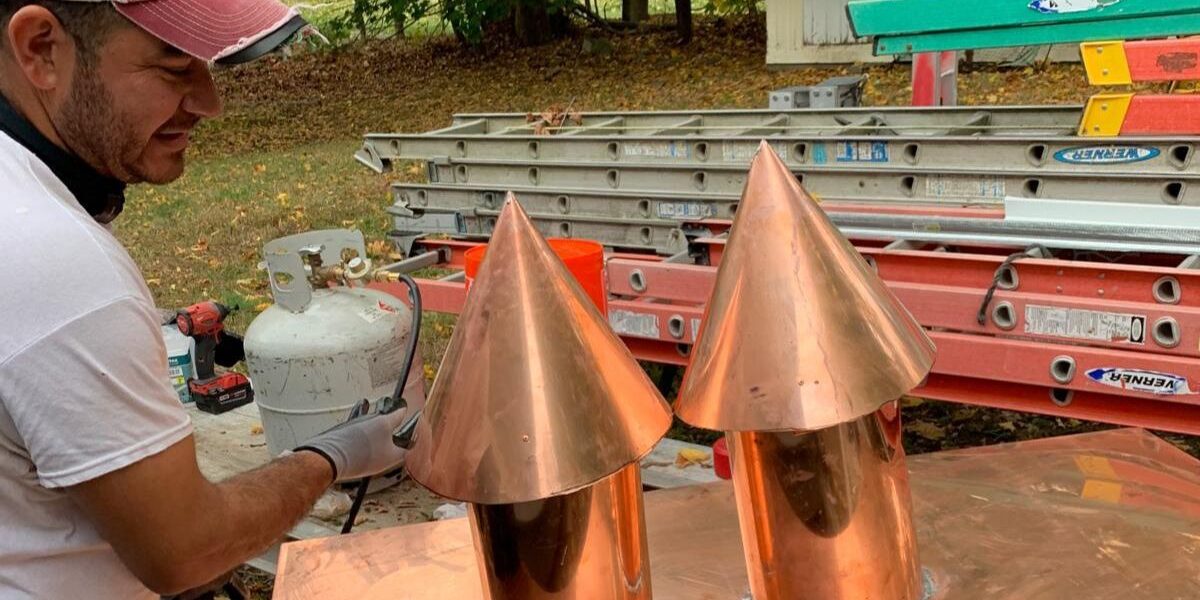 Luminous Construction craftsman soldering custom copper chimney caps for architectural roofing and flashing