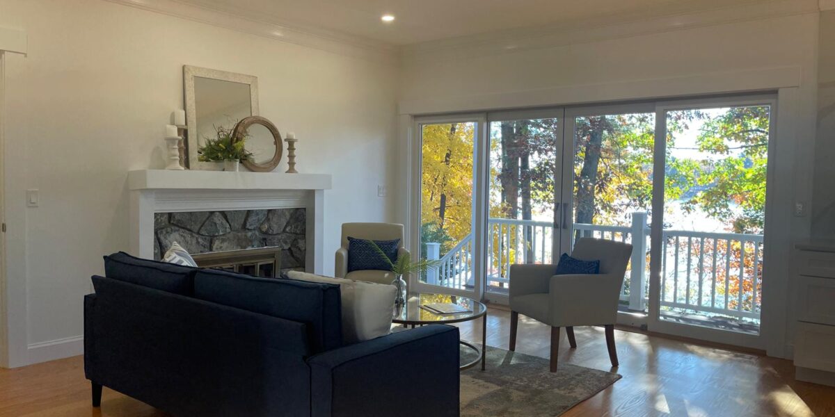 Living room renovation with stone fireplace, comfortable seating, and wide glass doors to the deck