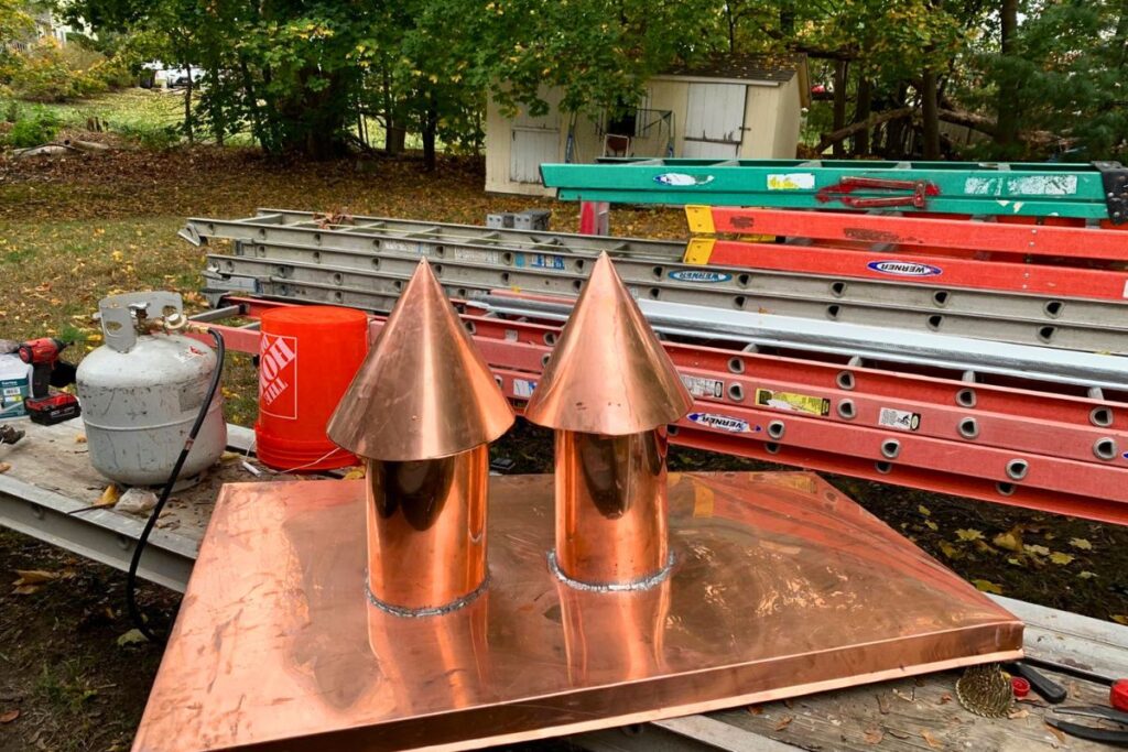Handcrafted double copper chimney cap installation for luxury residential exterior renovation in Massachusetts