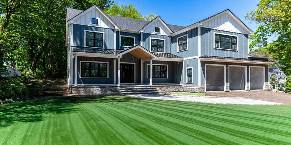 Modern luxury custom home exterior featuring blue siding, white trim, triple garage, and stone foundation in Weston MA