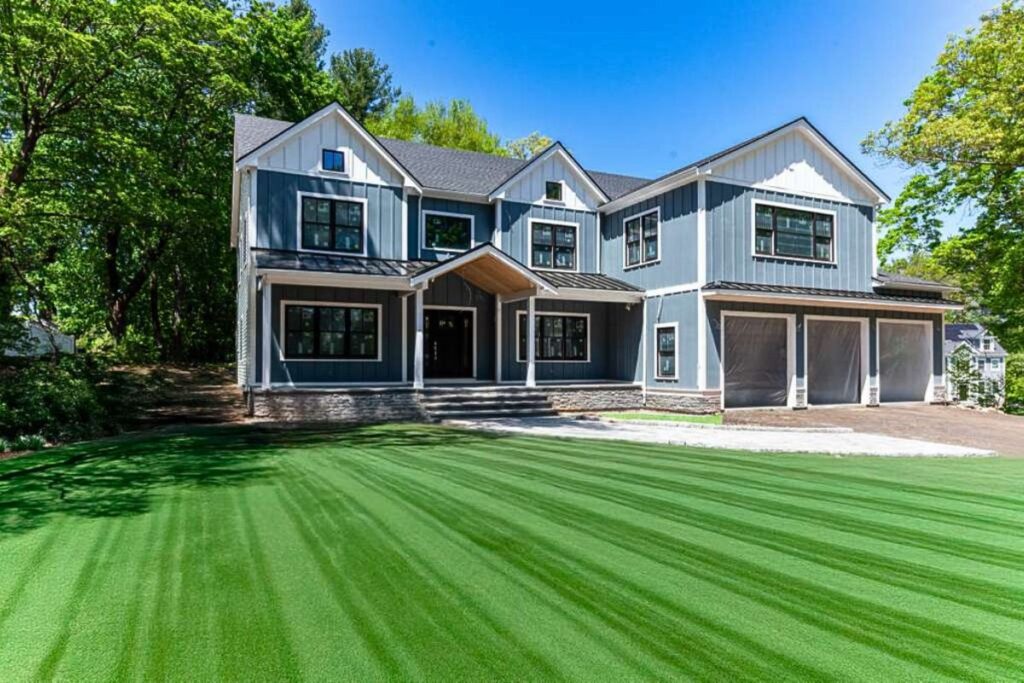 Luxury design build custom home in MA featuring blue architectural siding stone foundation and three car garage