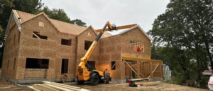 Heavy machinery lifting structural timber beams during custom home framing in Massachusetts