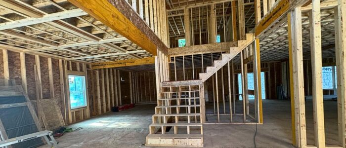 Interior view of a two-story residential wood framing project showing floor joists and staircase framing