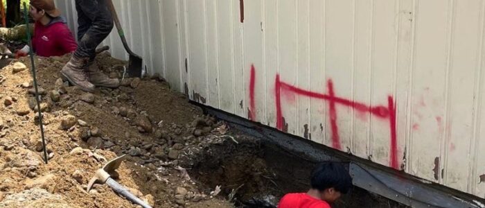 Construction crew digging and setting foundation underpinning beneath residential structure in Natick MA