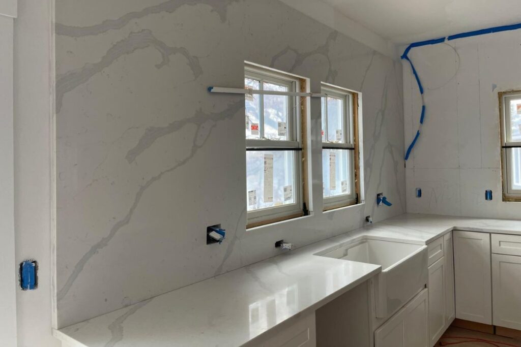 Precision installation of full height veined quartz slab backsplash and matching countertops in luxury kitchen remodel