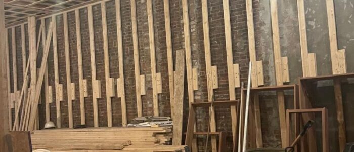 Complete gut renovation interior featuring raw brick walls, wood stud wall framing, and ceiling strapping