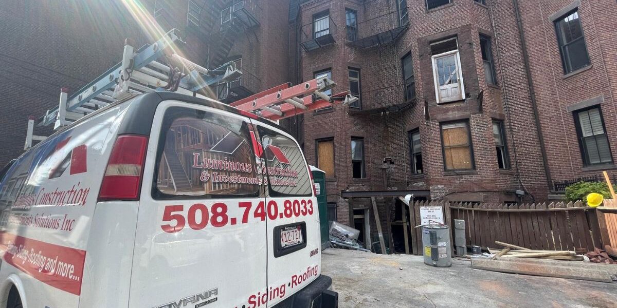 Luminous Construction service van parked at historic multi-story brick building restoration site in Sudbury MA