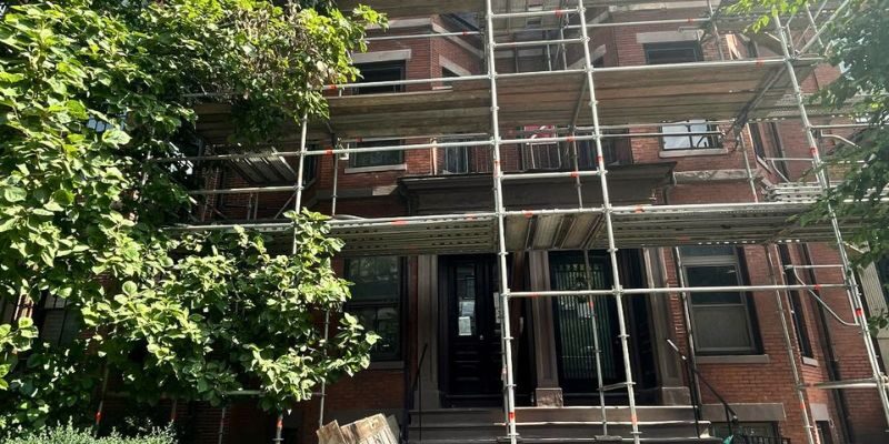 Historic brick building covered in protective netting and scaffolding during structural renovation