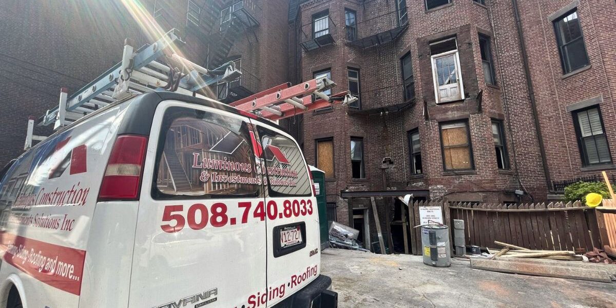 Luminous Construction service van parked outside a historic brick building restoration site in Massachusetts