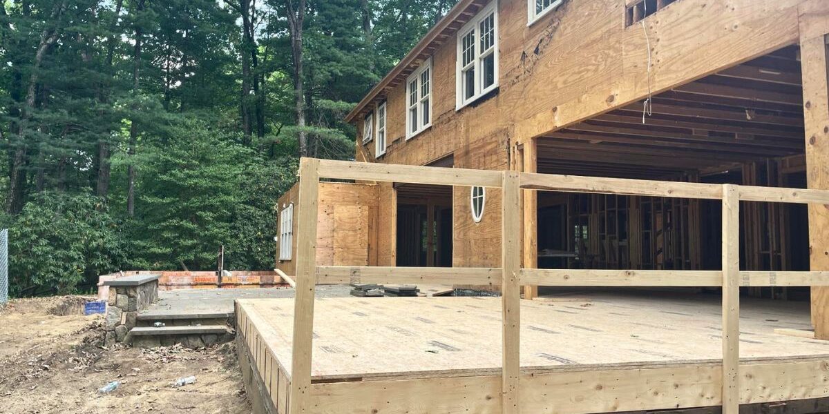 Rear view of a luxury residential home addition showing subflooring framing and stone patio steps in Wellesley MA