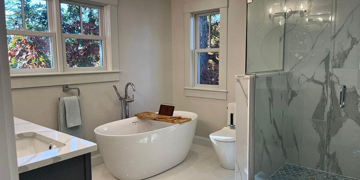 Master bathroom remodel with dark grey vanity, white quartz countertop, freestanding tub, and marble shower enclosure in Natick MA